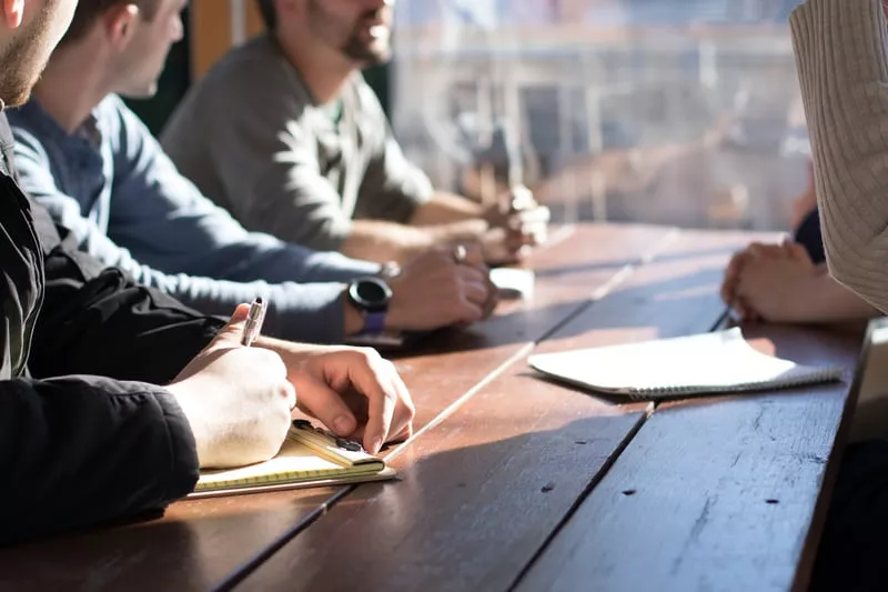 Photo d'une équipe de cinq personnes en réunion autour d'une table avec un homme qui prend des notes